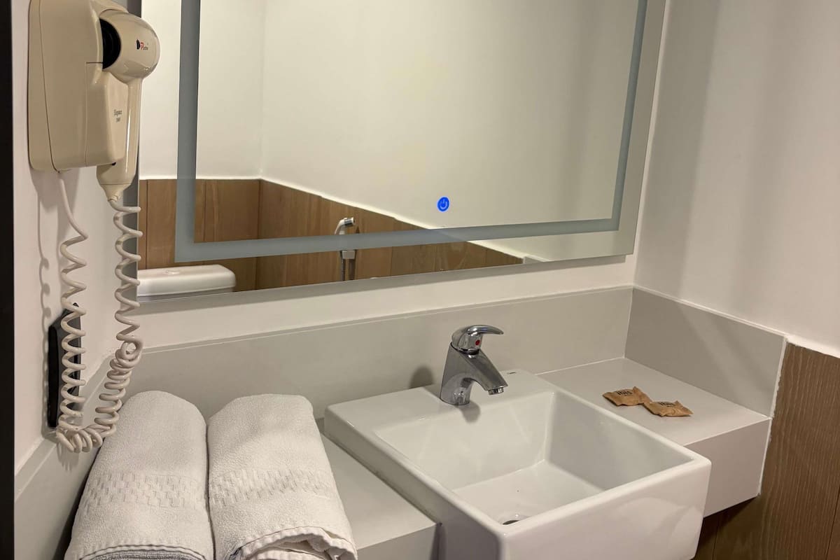 A bathroom with a white sink, a mirror, a hair dryer, and neatly folded towels.