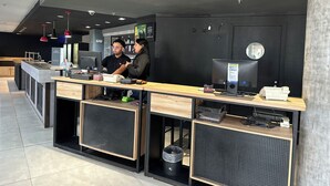 A modern reception desk with a computer, a cash register, and a small trash bin. - Ibis Joao Pessoa (João Pessoa)