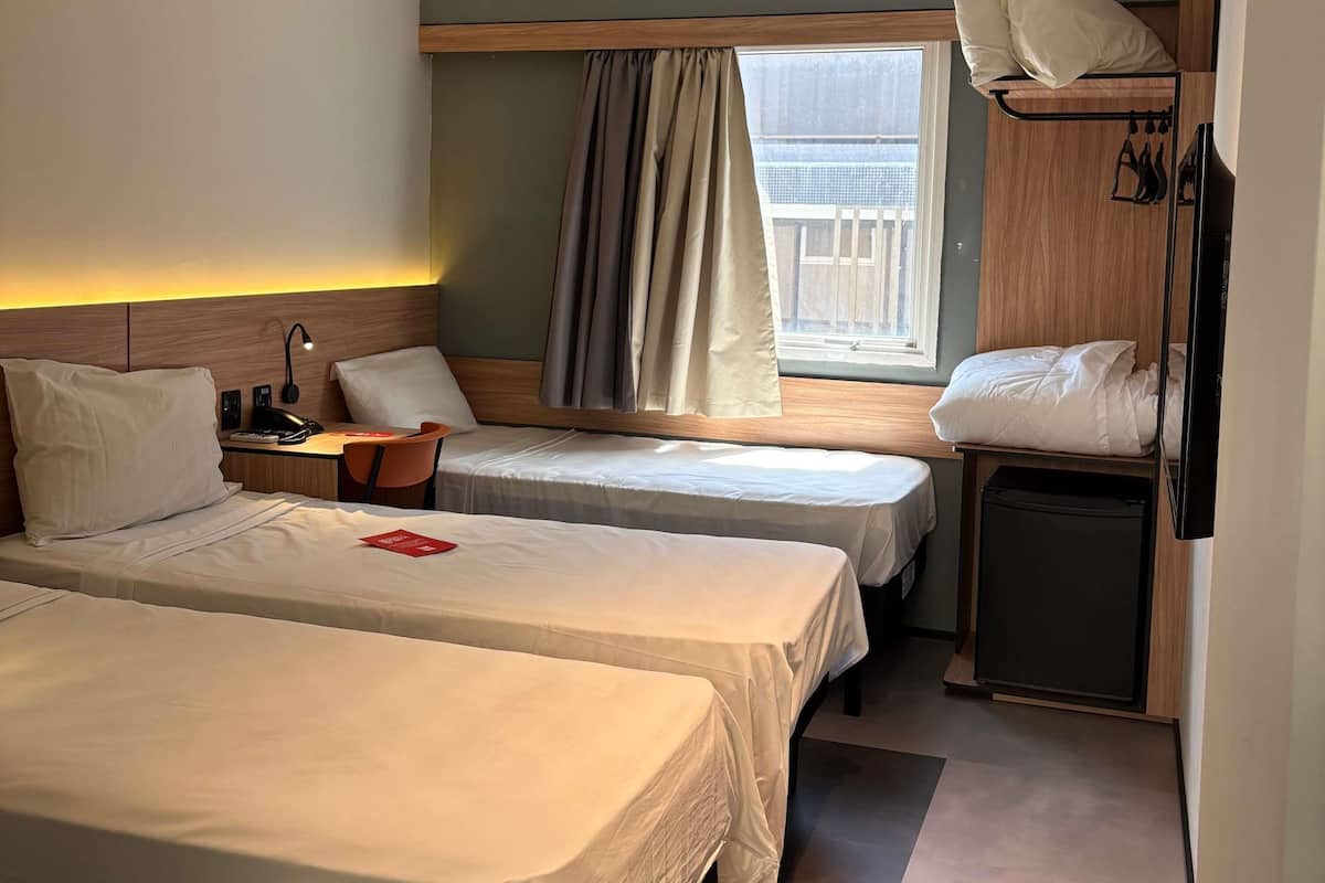 A hotel room with two beds, a desk, a chair, a TV, and a window with curtains.