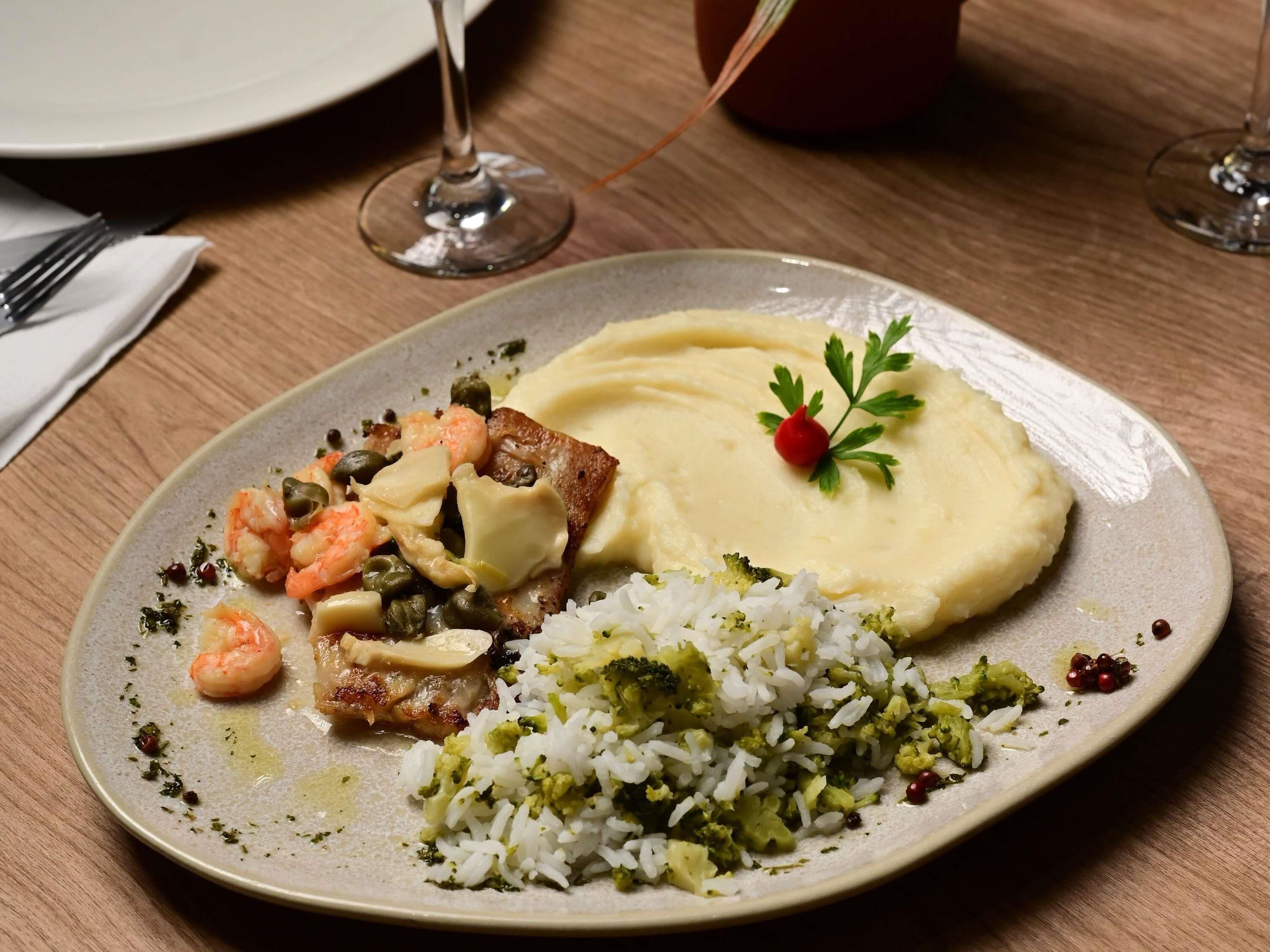 A plate with rice, broccoli, shrimp, and a piece of meat, possibly chicken, on a wooden table.