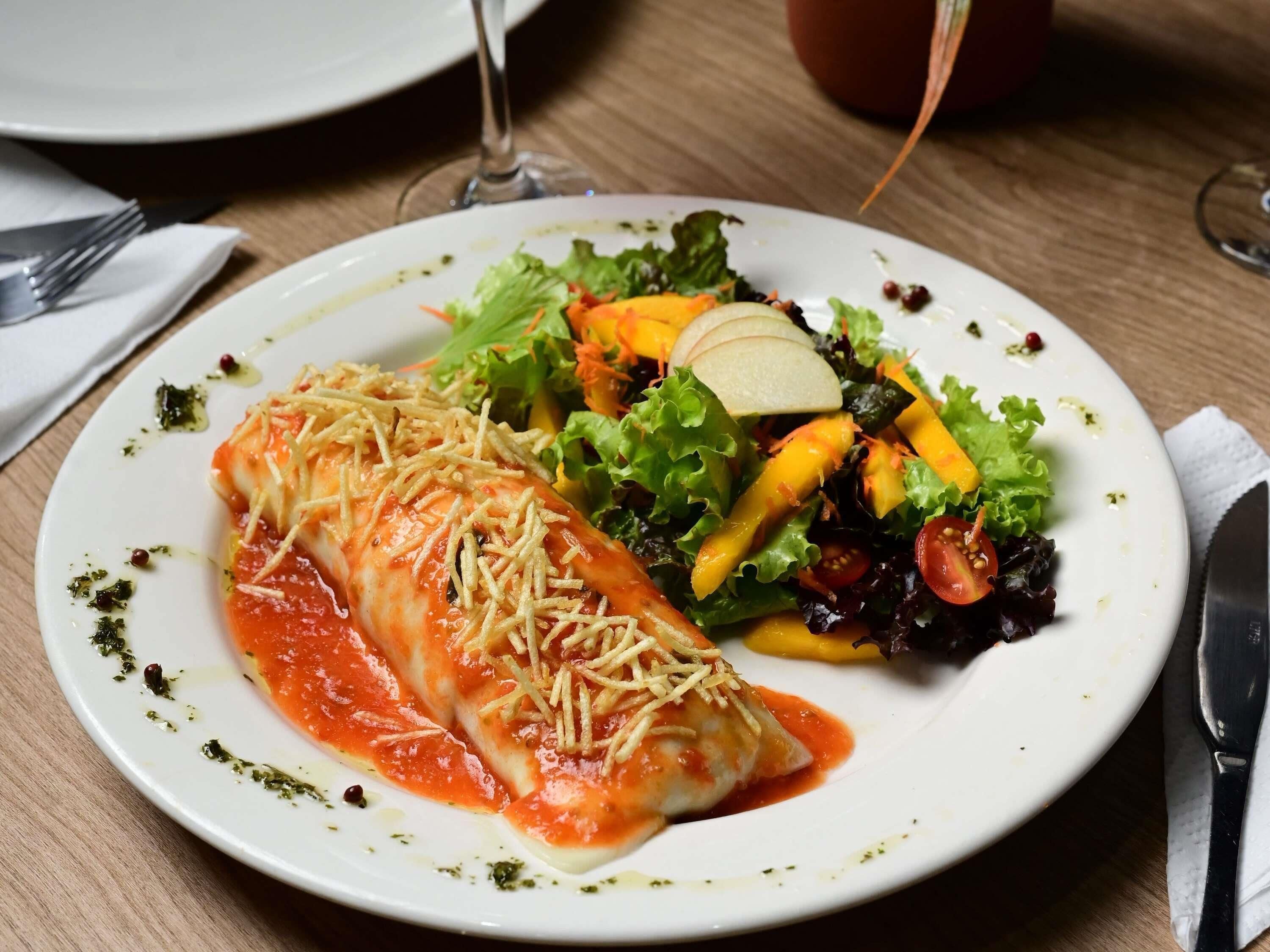 A plate with a rolled dish, a salad, and a glass of red wine on a wooden table.