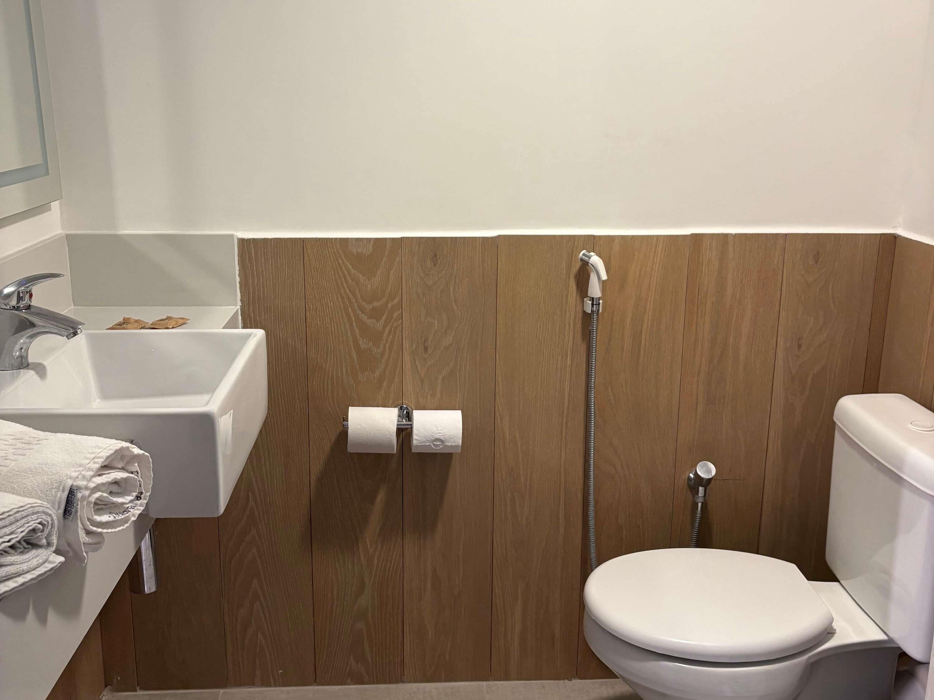 Um banheiro com parede de painel de madeira, pia branca, vaso sanitário e chuveiro.
