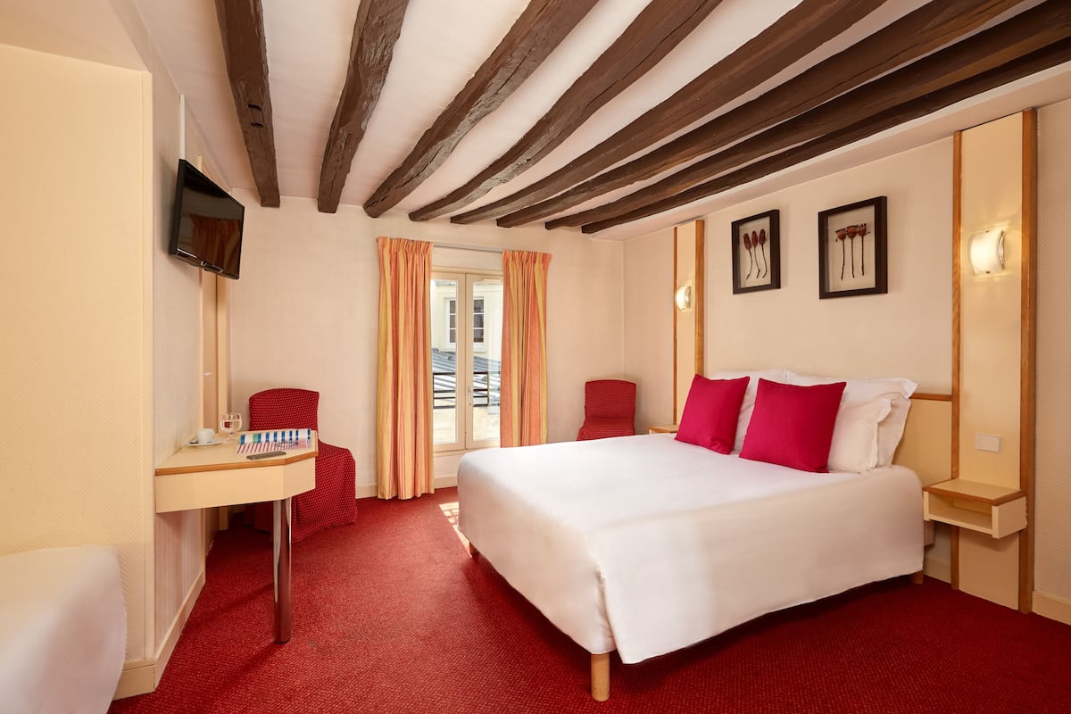 A hotel room with a bed, a desk, a chair, and a TV mounted on the wall.