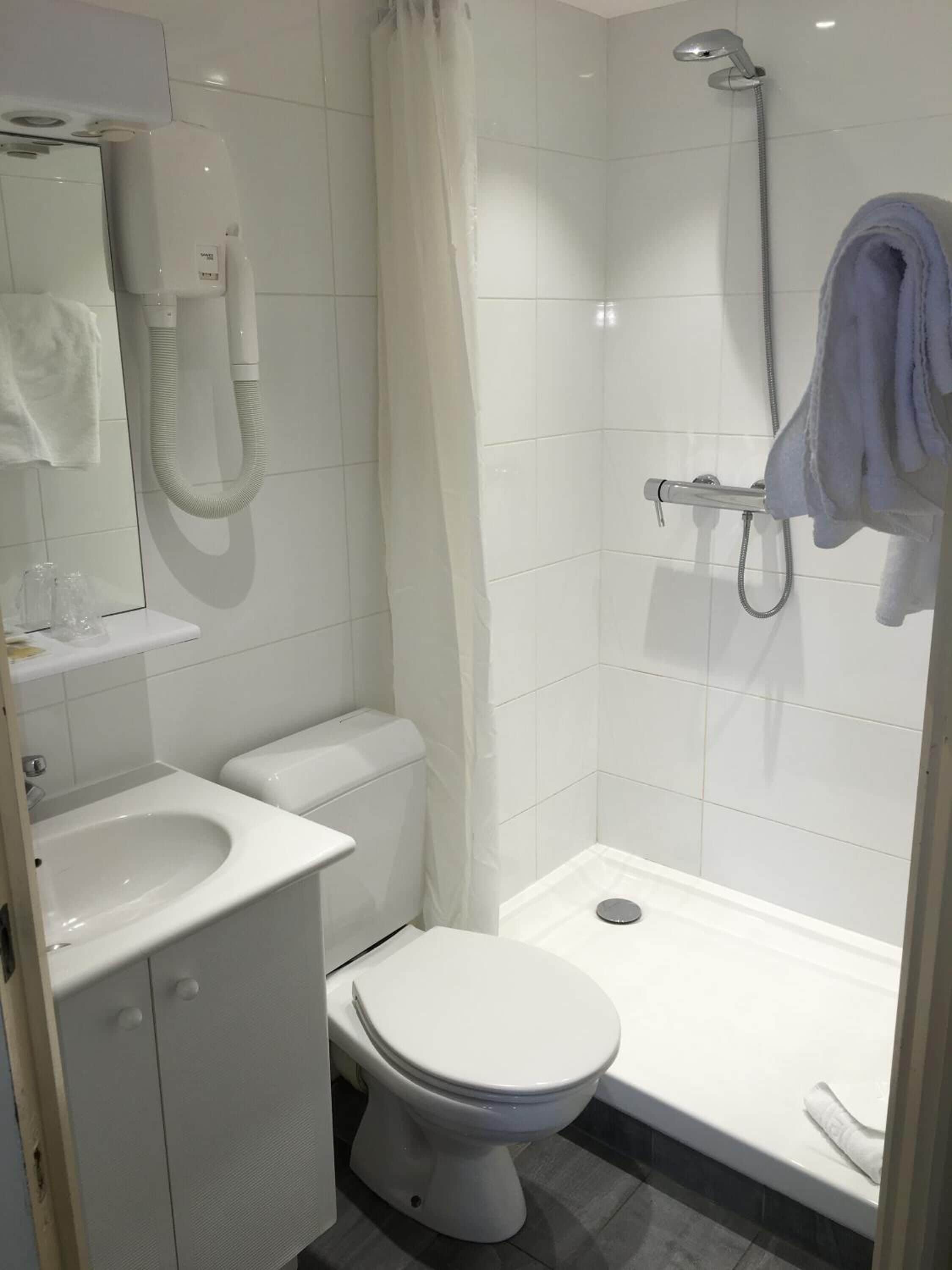 Egy kis, tiszta fürdőszoba, amelyben WC, mosdókagyló és zuhanyzó található.