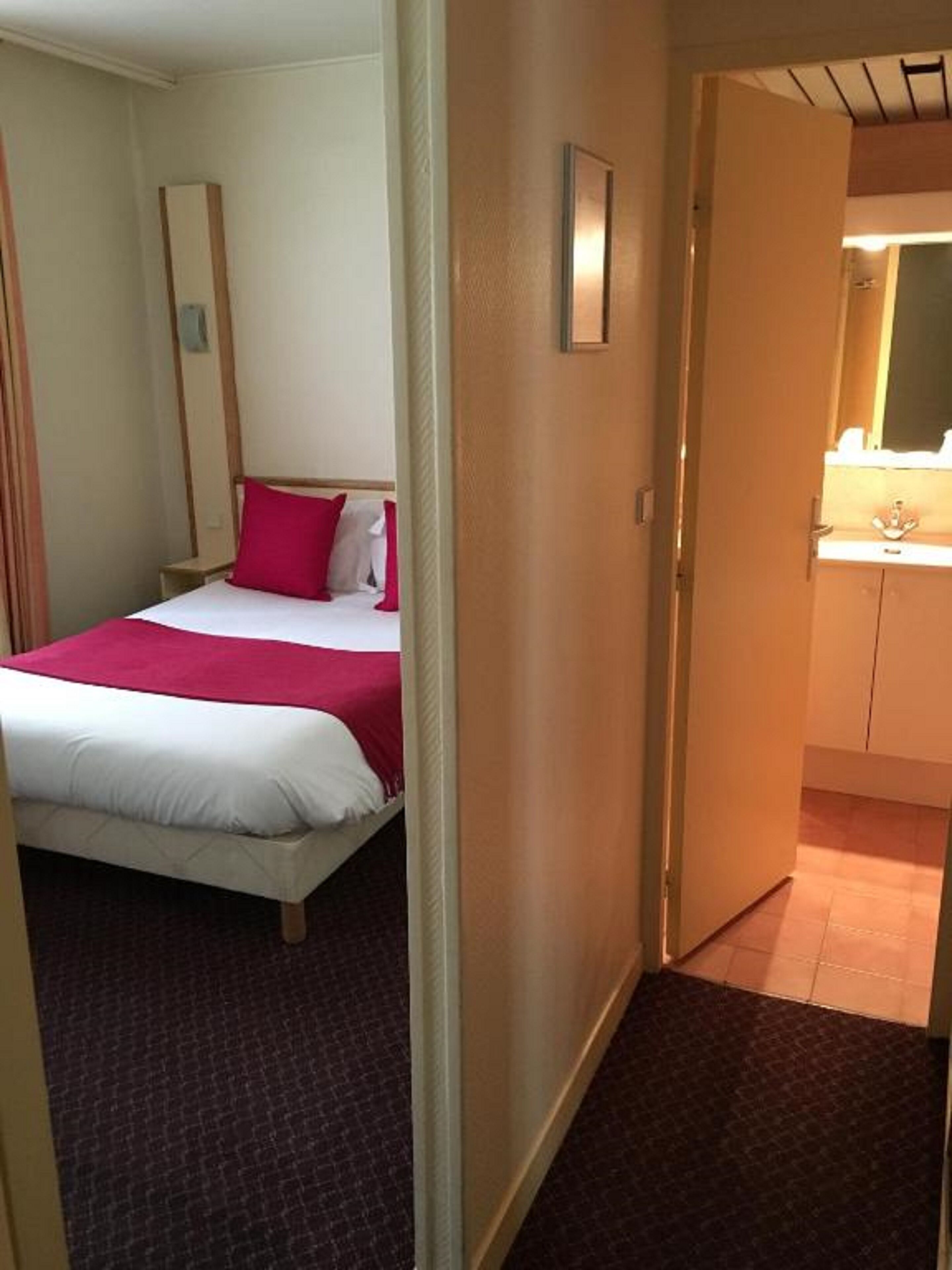 A hotel room with a bed, a nightstand, a mirror, and a bathroom visible through an open door.