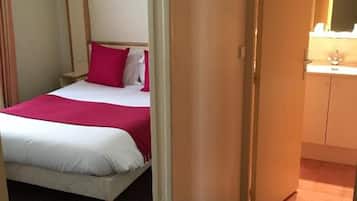 A hotel room with a bed, a nightstand, a mirror, and a bathroom visible through an open door.
