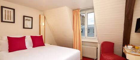 A hotel room with a bed, a red chair, a small table with breakfast items, and a window with curtains.