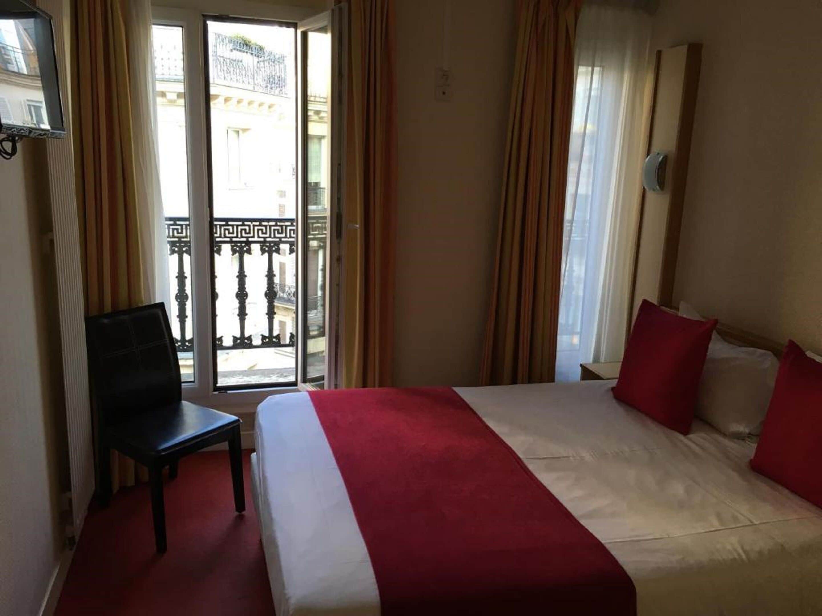 A hotel room with a bed, a chair, and a view of a balcony with a railing.