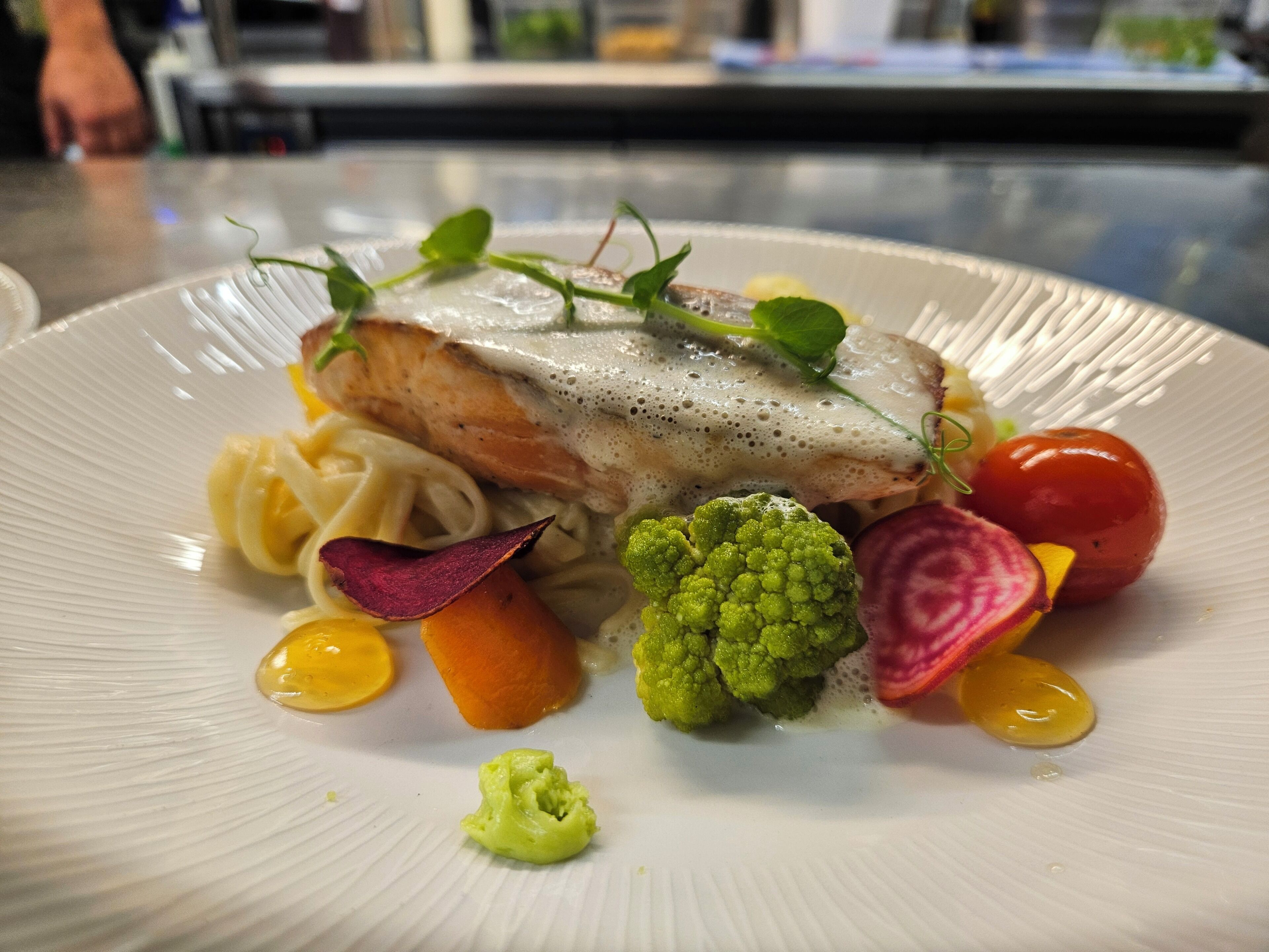 Un plato de comida con un filete de pescado, verduras y fideos.