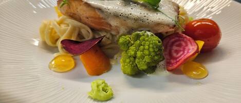 Un plato de comida con un filete de pescado, verduras y fideos.