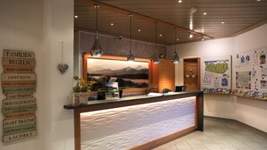 A reception desk with a landscape painting, hanging lights, and a bulletin board with various notices. - Dei Hotel Schönblick (Velden am Wörther See)