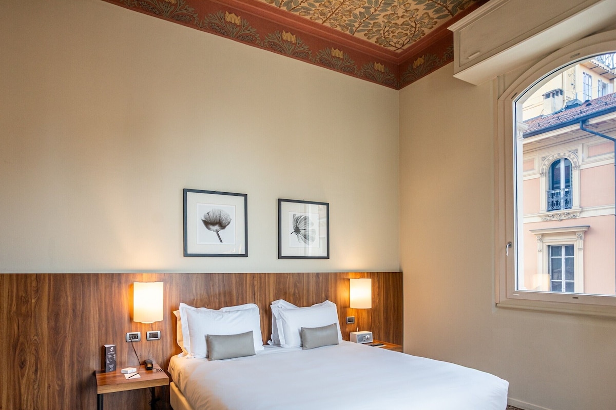 Una habitación de hotel con una cama grande, dos mesitas de noche con lámparas y dos cuadros en la pared.