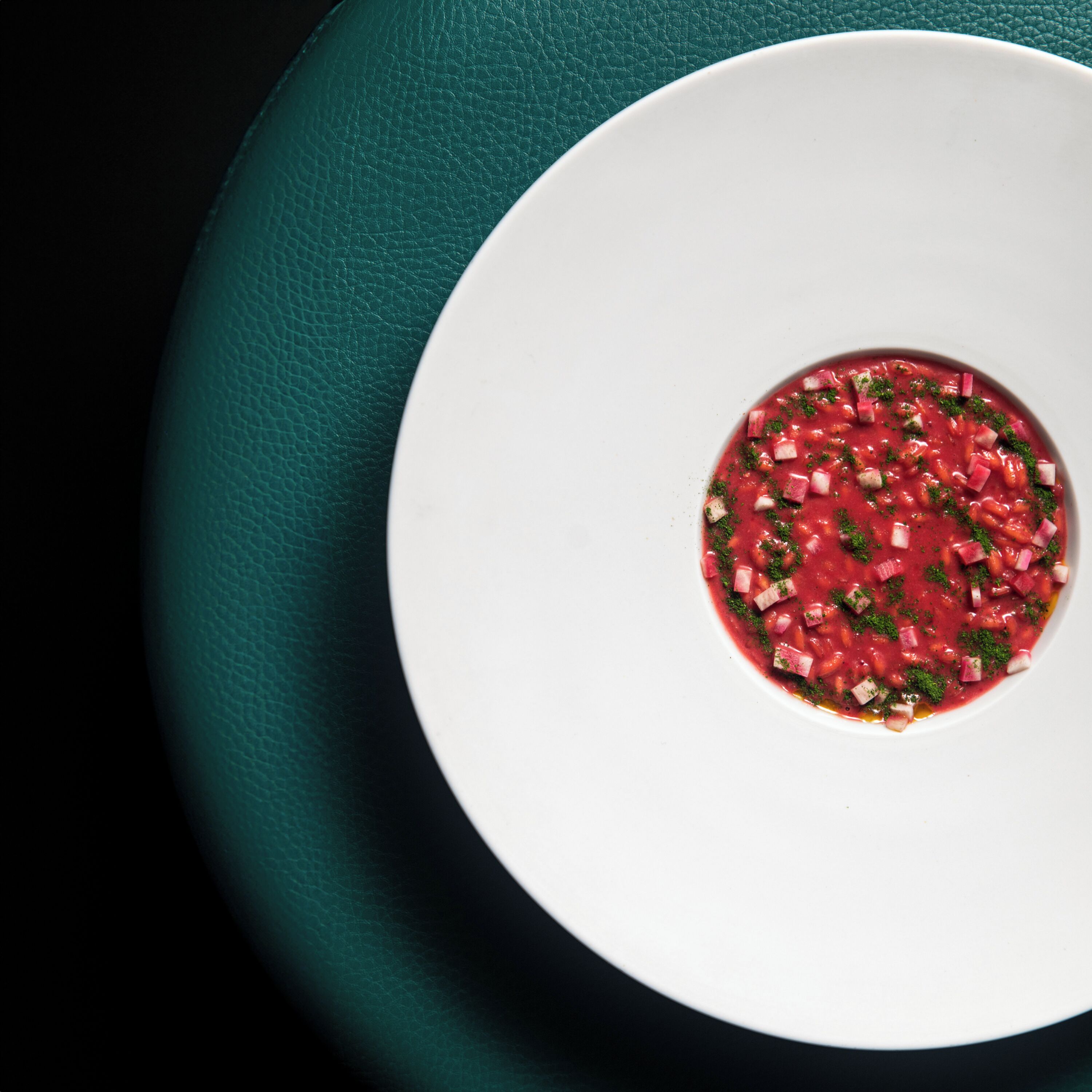 Un bol blanc contenant une soupe avec des légumes coupés en dés et des herbes, posé sur une surface vert foncé.