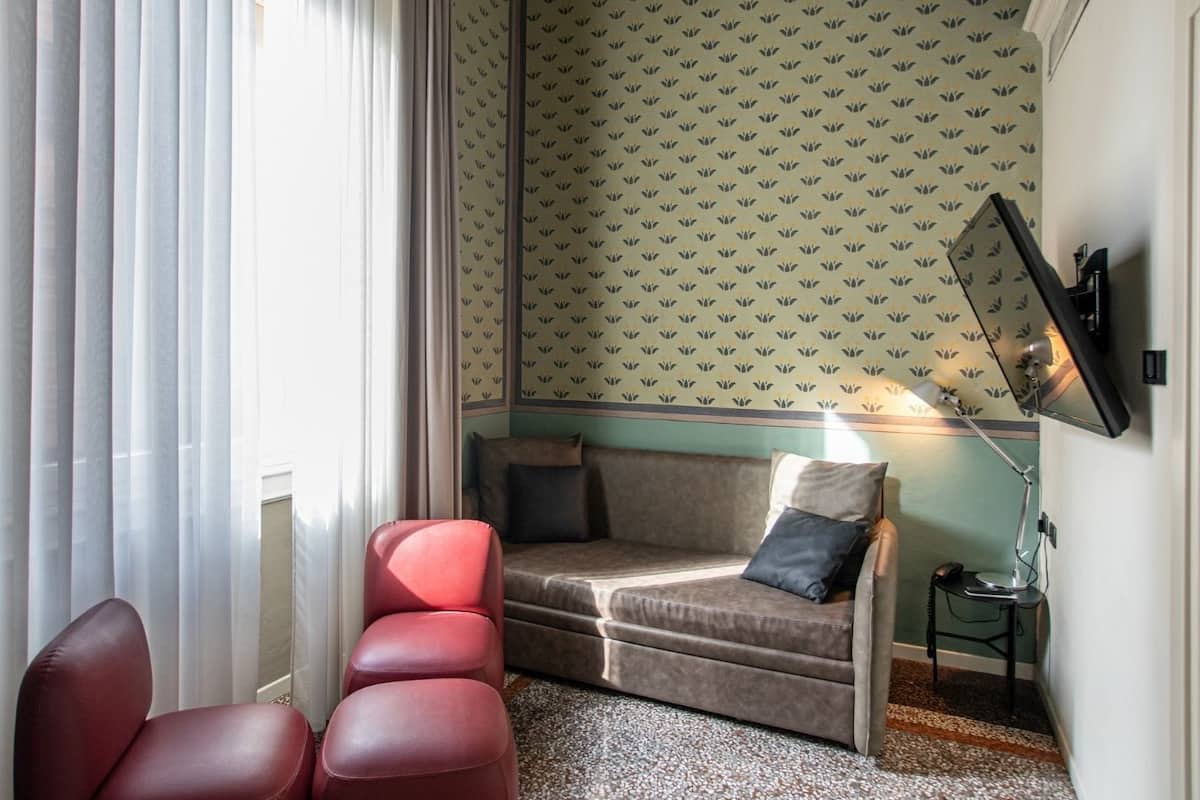 Huoneessa on sohva, kaksi punaista tuolia, pieni pöytä, jossa on lamppu, ja seinälle asennettu televisio.
