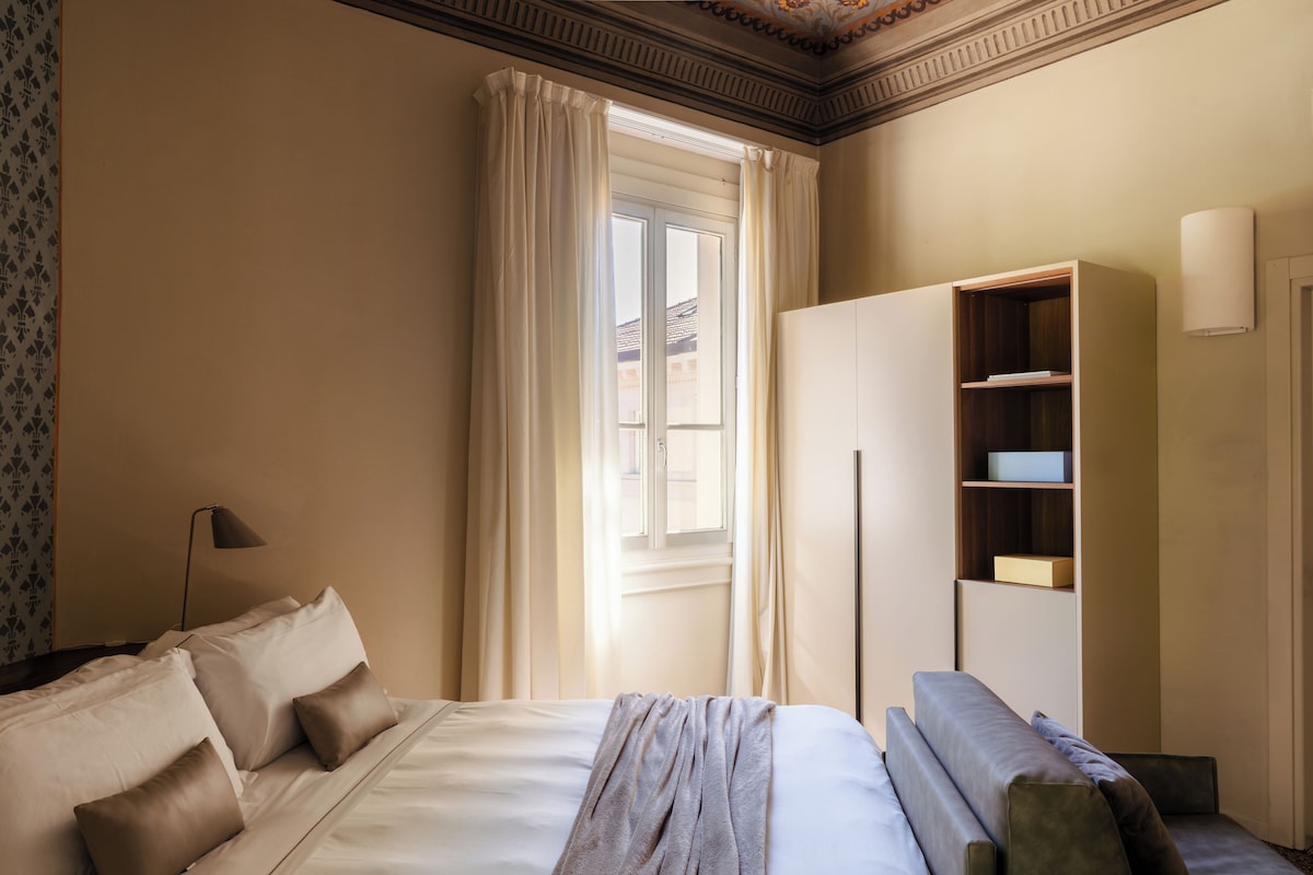 Una habitación de hotel con cama, armario, escritorio y ventana con cortinas.