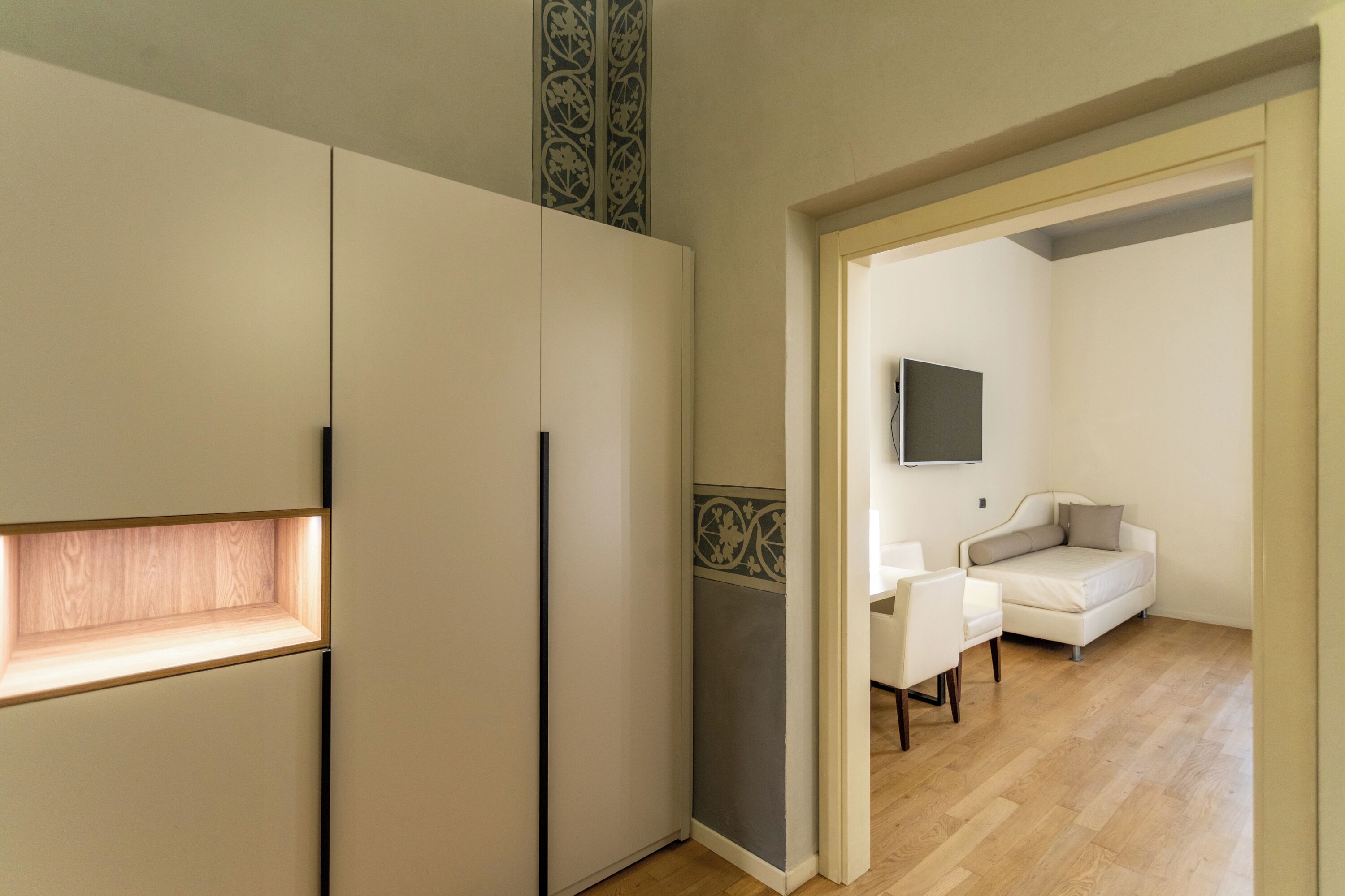 Un interno moderno con pavimento in legno, un divano bianco e un televisore a schermo piatto montato a parete.