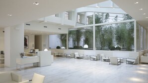 Amplia y moderna zona de recepción con techos altos y grandes ventanales con vistas a un jardín de bambú.