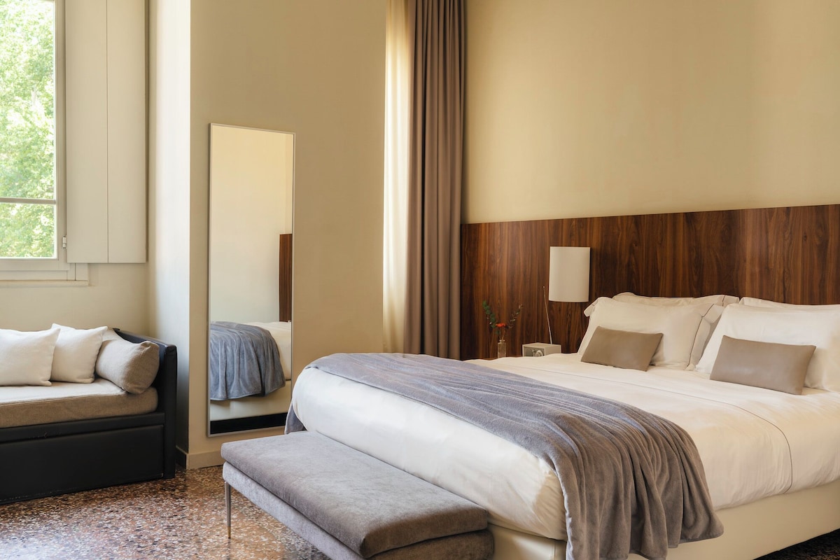 Habitación de hotel con cama, un banco, un espejo y un cabecero de madera.