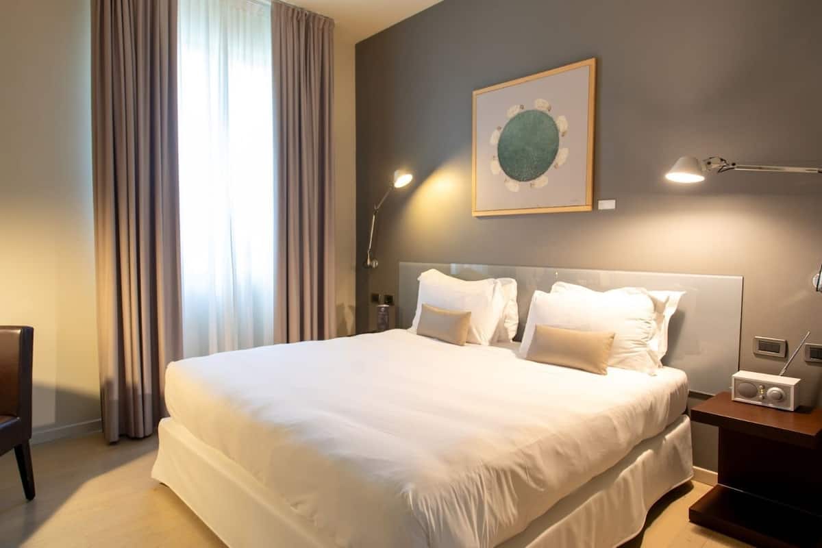 Hotellihuone, jossa on suuri sänky, työpöytä tuolilla, yöpöytä lampun kanssa ja taulu seinällä.
