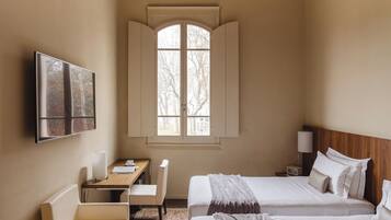 Una habitación de hotel con una cama, un escritorio con silla, televisión y ventana con persianas.
