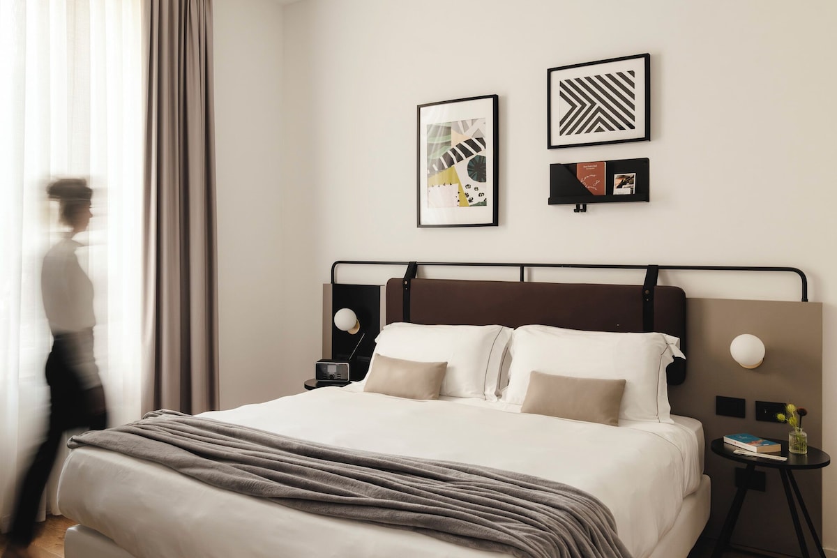 Una habitación de hotel con una cama, mesitas de noche y obras de arte en las paredes.