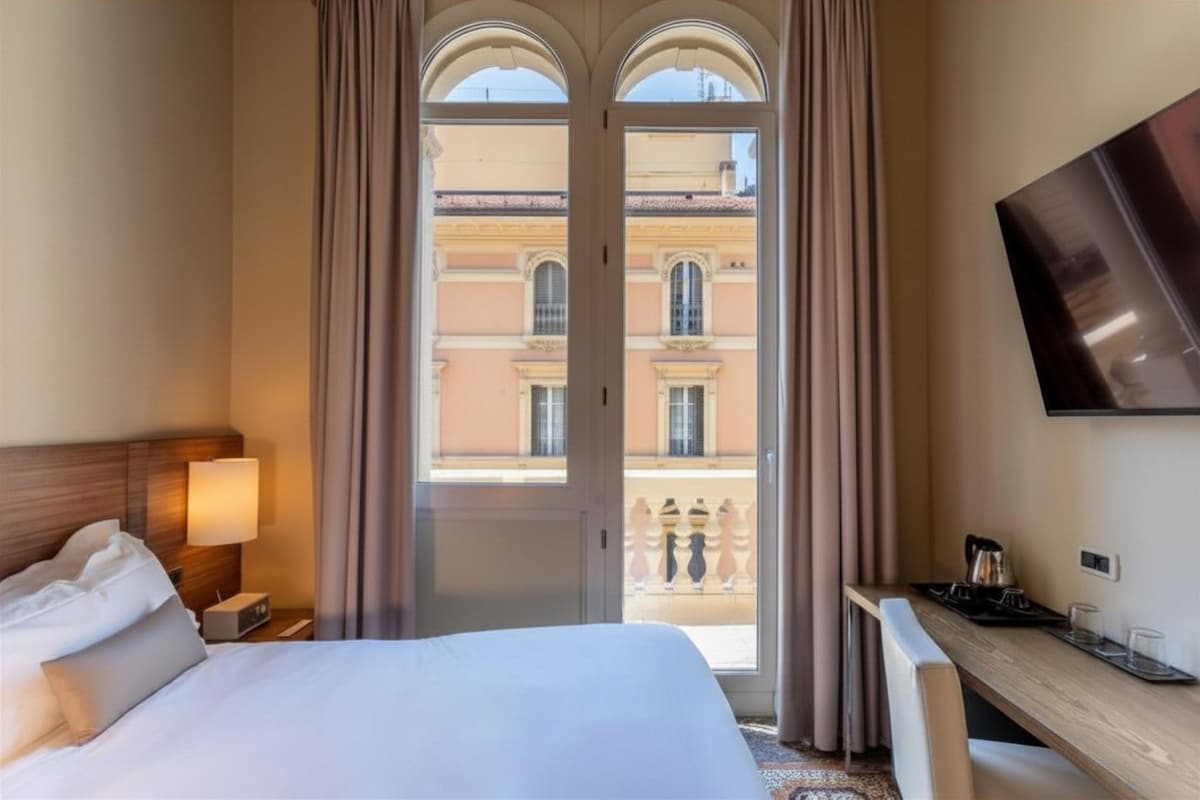 Habitación de hotel con cama, escritorio, televisión y vista a un edificio a través de una puerta.