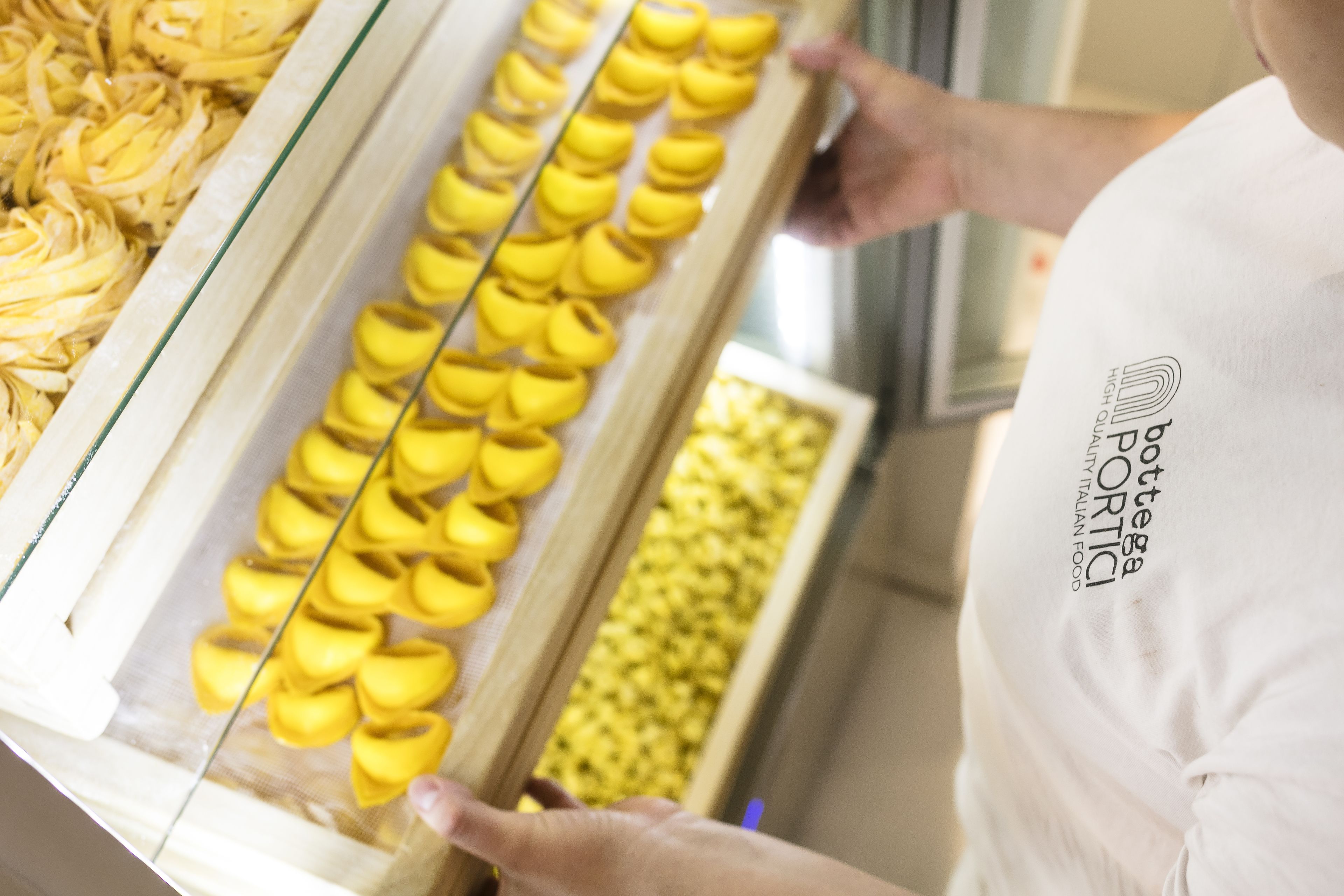 A person holding a tray with yellow pastries, possibly cannoli, in a bakery setting.