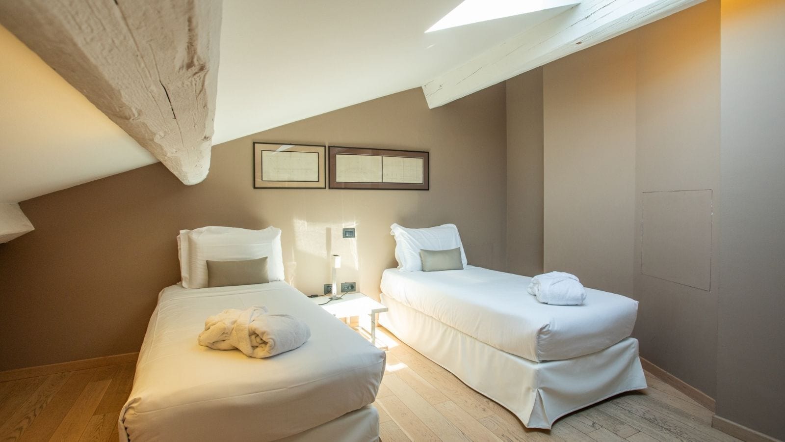 Una camera da letto accogliente e piccola con due letti singoli, un lucernario e due cornici appese al muro.