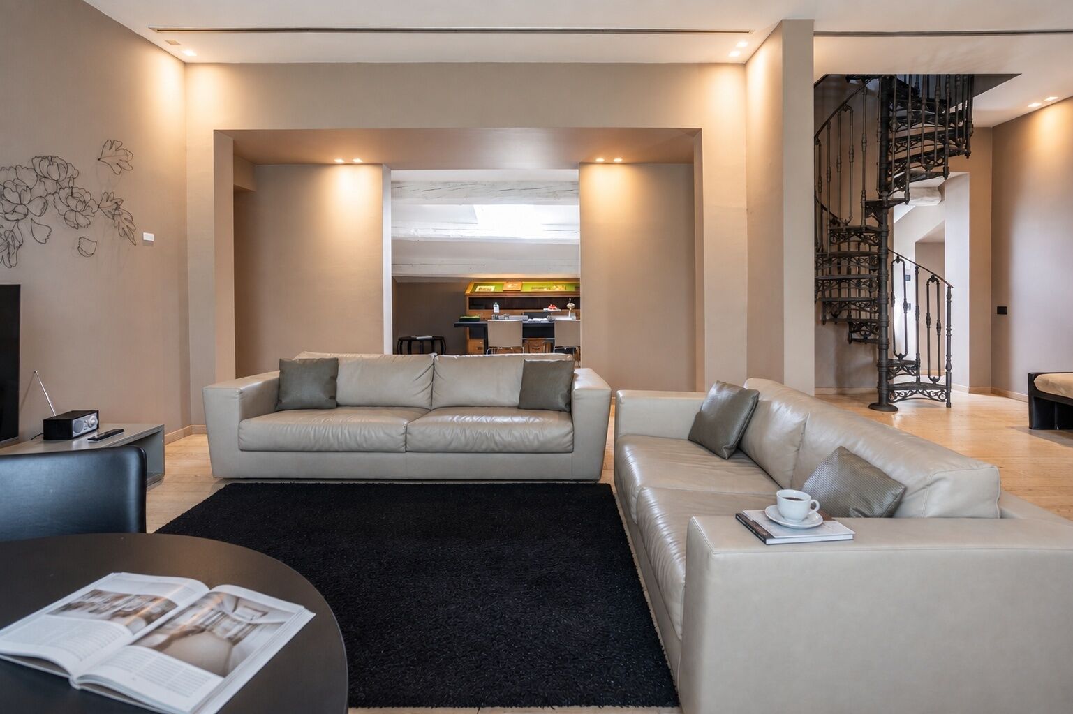 Uma sala de estar moderna com um sofá, uma mesa de centro e uma estante. Há uma escada com um corrimão decorativo que leva a um andar superior.