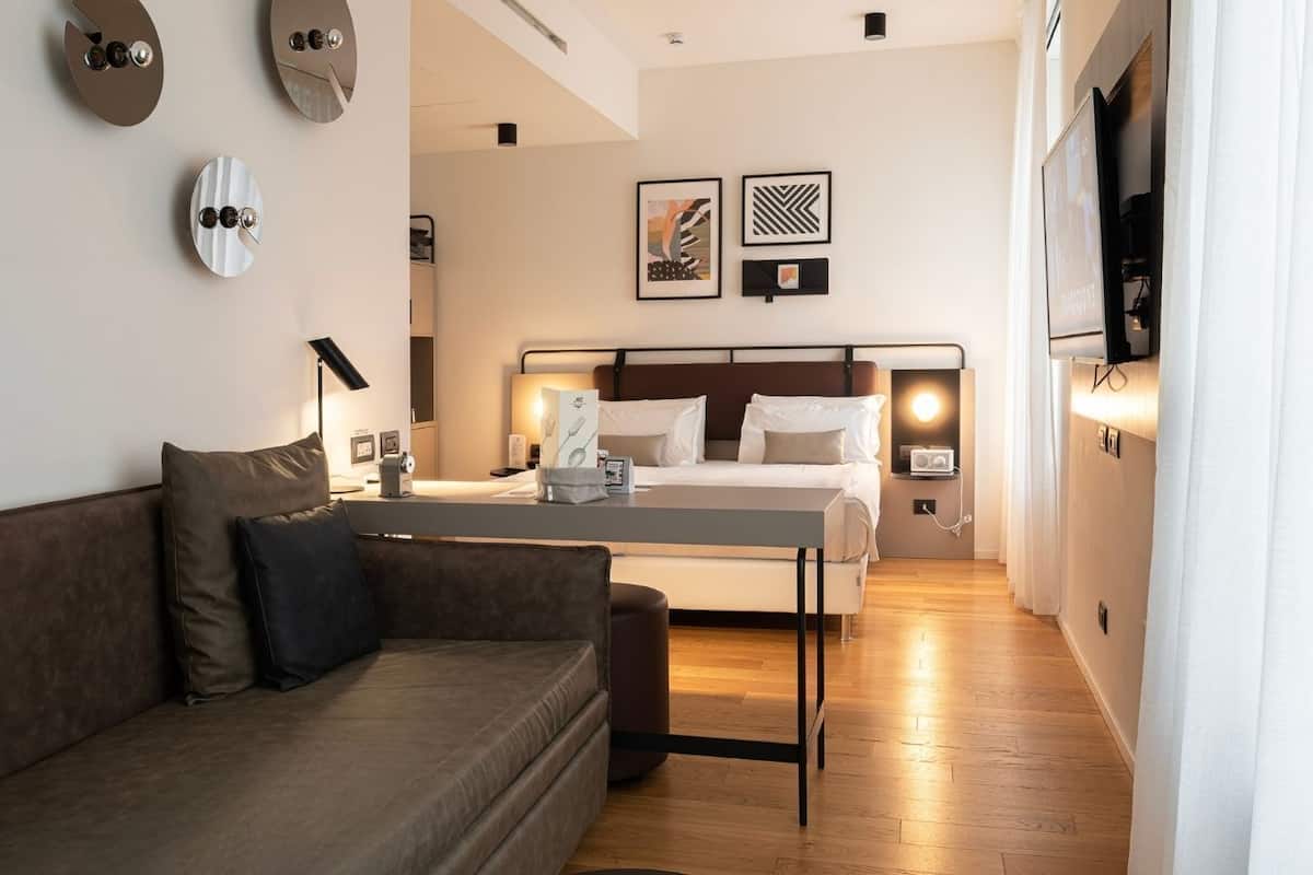 Moderni hotellihuone, jossa on sohva, sänky, yöpöytä ja taulutelevisio.
