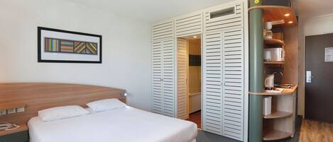 Habitación de hotel con cama, armario y una pequeña cocina.