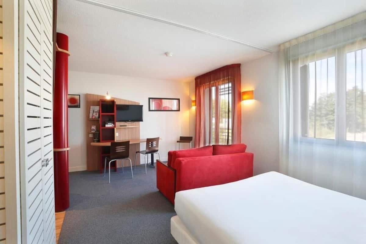 A hotel room with a bed, a desk, a chair, and a TV.