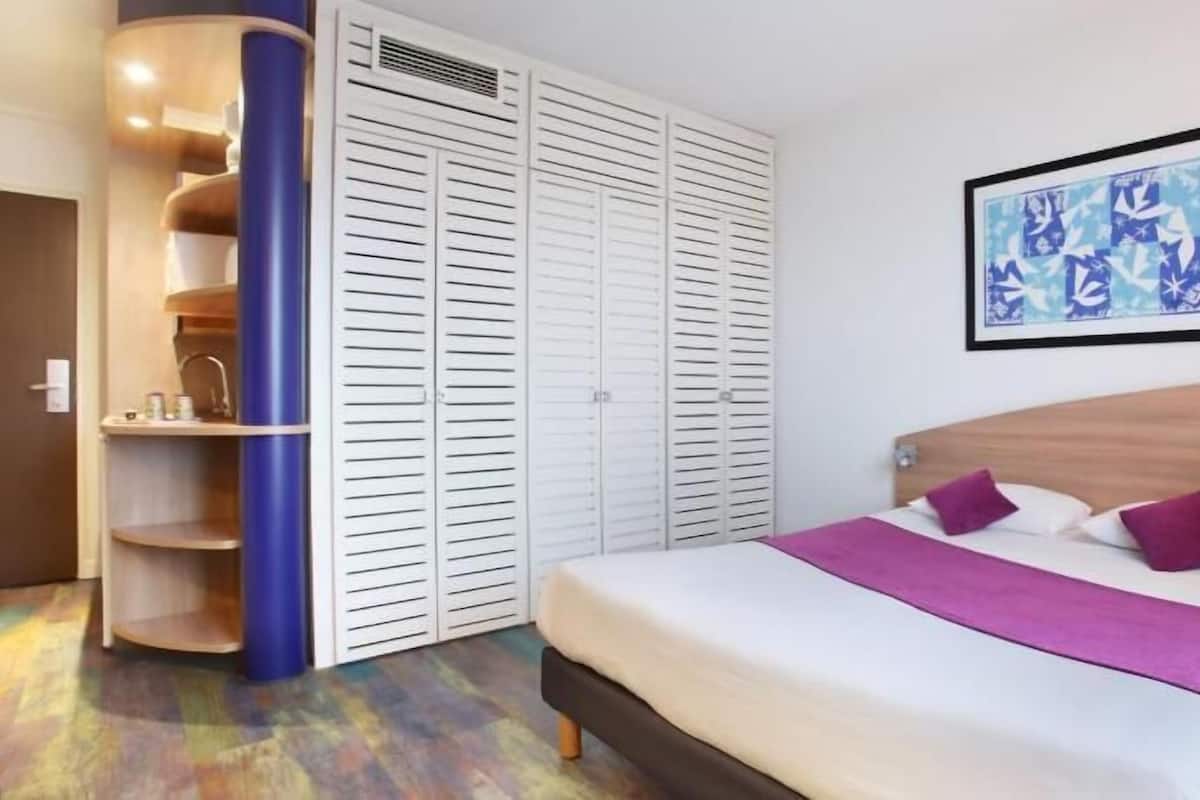 A hotel room with a bed, a wardrobe, a sink, and a framed picture on the wall.