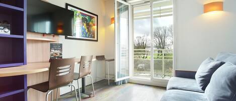 Una sala de estar moderna con un sofá, un televisor montado en la pared, un comedor con sillas y un amplio ventanal con vistas al exterior.