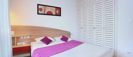 Una cama bien hecha con ropa de cama blanca y morada, un cabecero de madera y una obra de arte colgada en la pared.