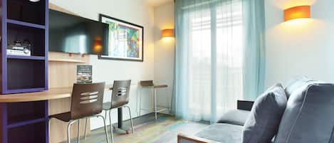 Una sala de estar moderna con un sofá, un televisor instalado en la pared, un comedor con sillas y una estantería.