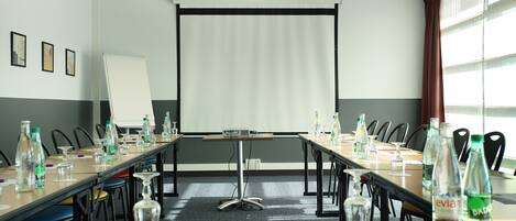 Un salón de conferencias con una larga mesa, sillas, una pantalla de proyector y botellas de agua.
