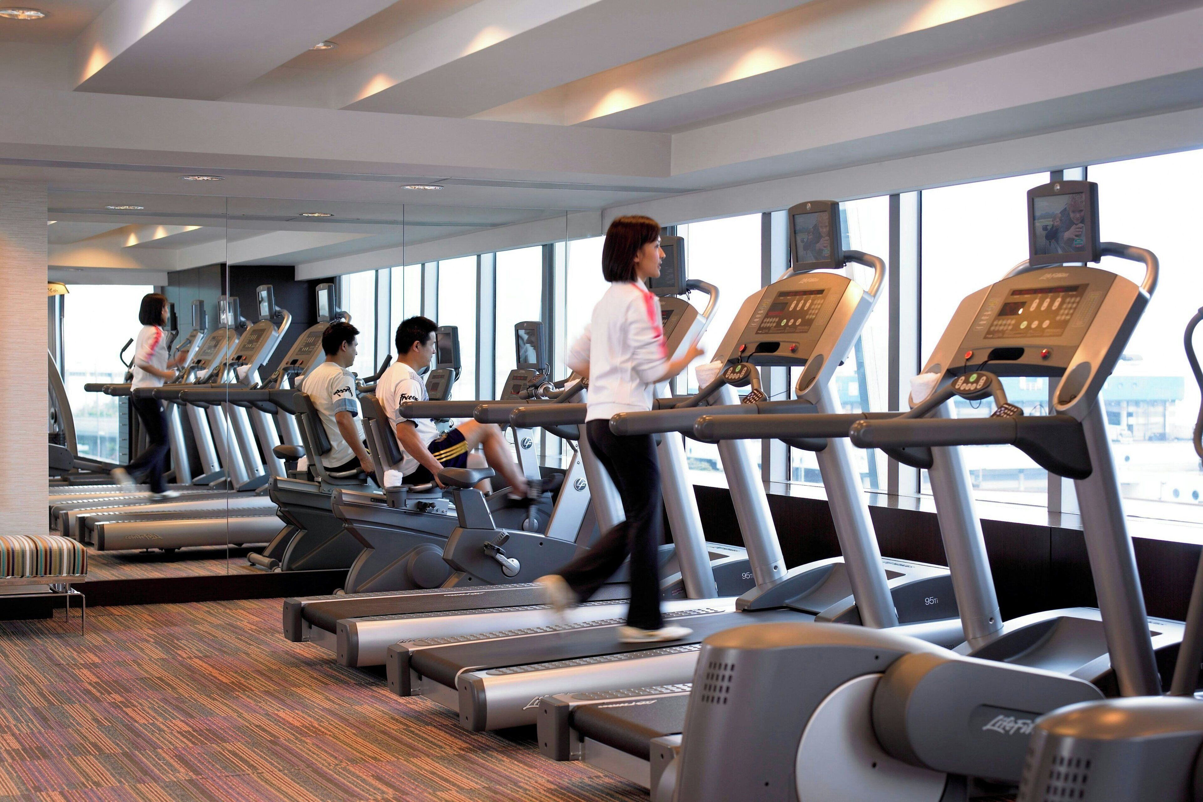 Un gimnasio con cintas de correr, equipo de ejercicio y amplias ventanas con vistas.