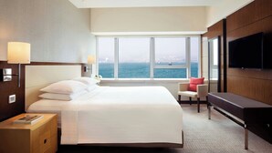 A hotel room with a large bed, a desk, a chair, a TV, and a view of the sea. - Courtyard by Marriott Hong Kong (Hong Kong)