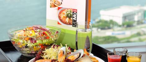 Una bandeja con ensalada, sushi y un menú de bebidas, frente a una vista panorámica de la ciudad.