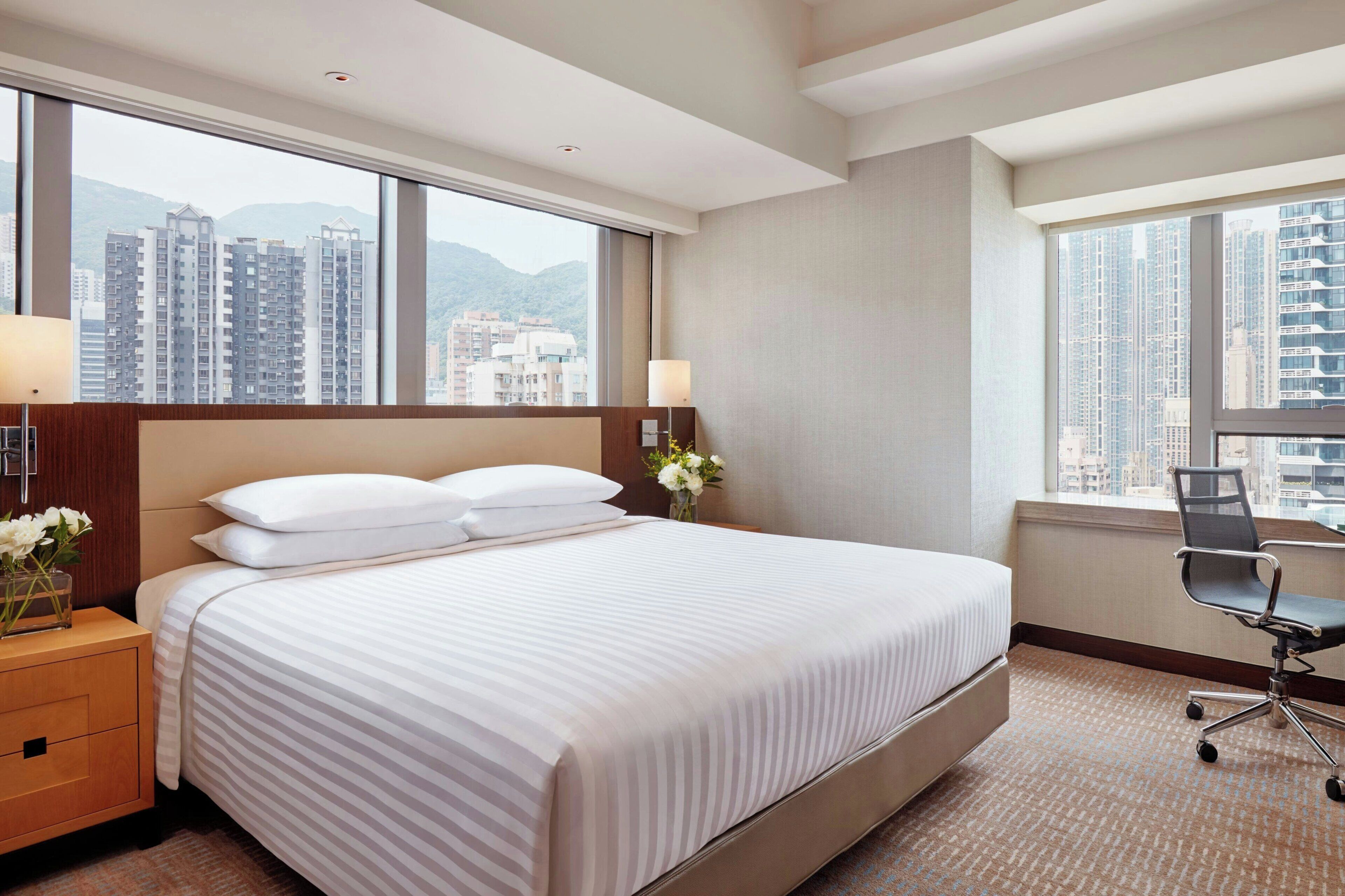 Quarto de hotel com uma cama grande, uma mesa e vista para edifícios altos.