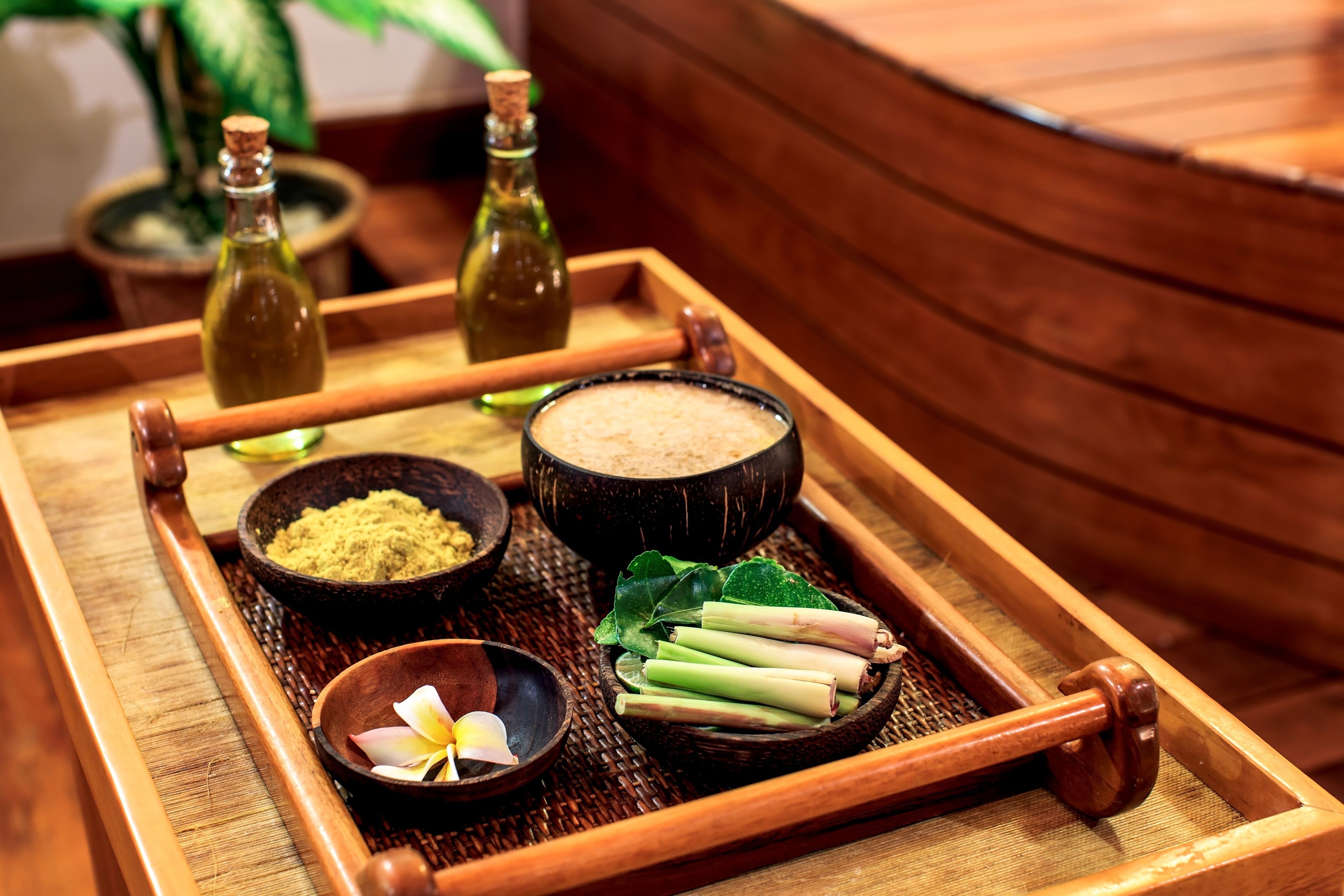 A wooden tray with various items including a bowl of green powder, a bowl of white powder, a bowl with a flower, and some green leaves.