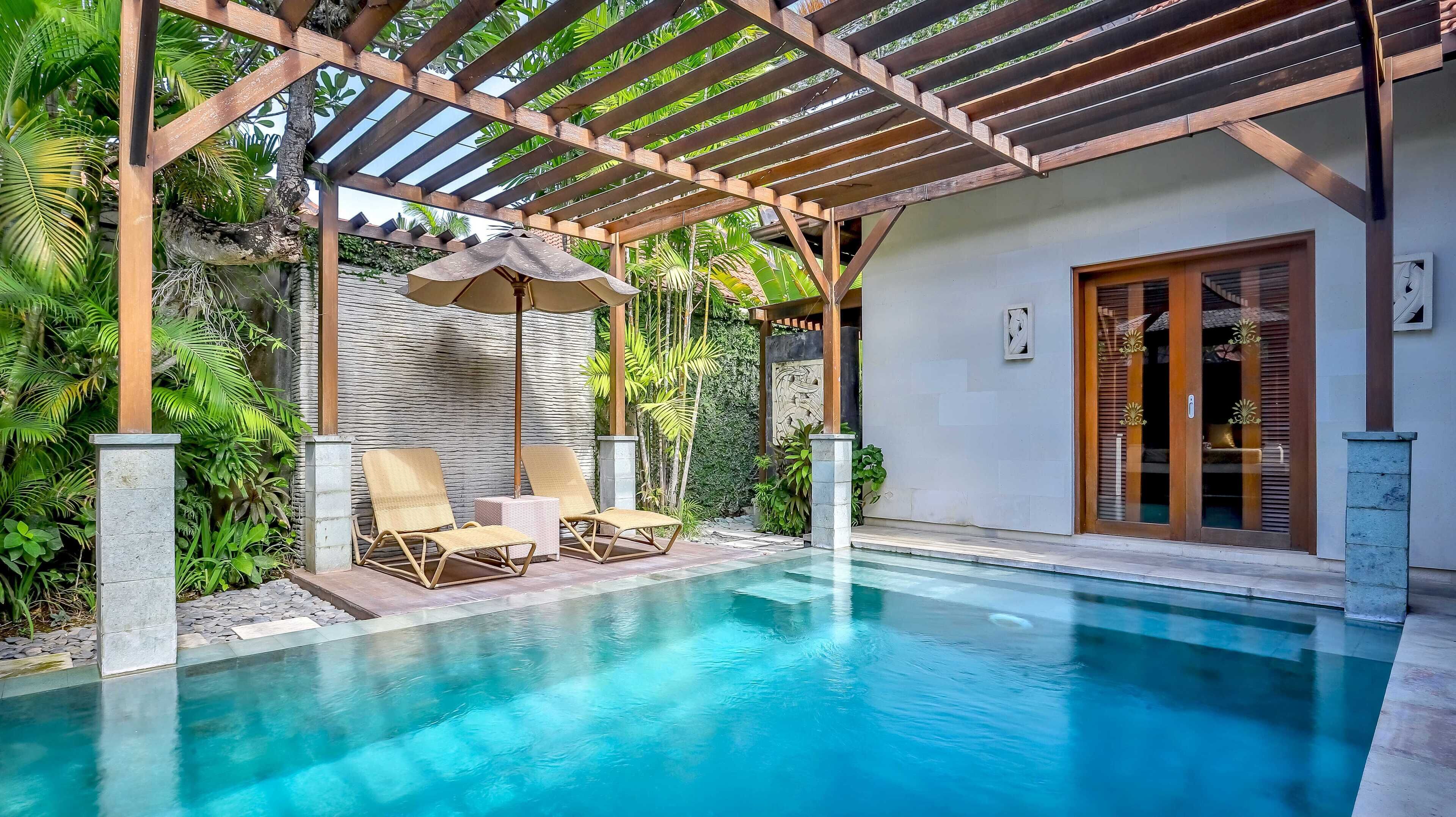 A pool area with two lounge chairs and a pergola overhead.