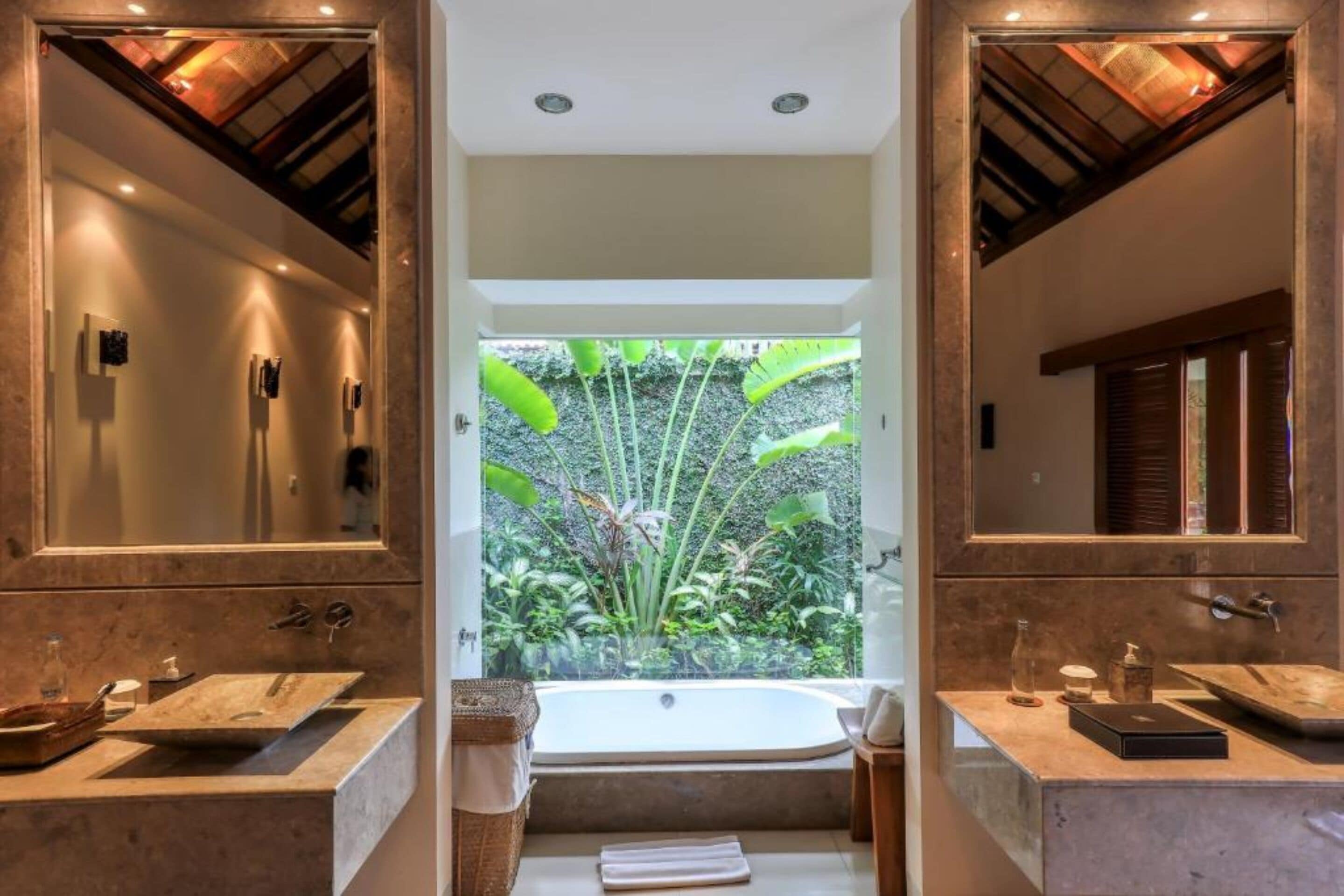 A bathroom with two sinks, a bathtub, and a large window with a view of greenery.