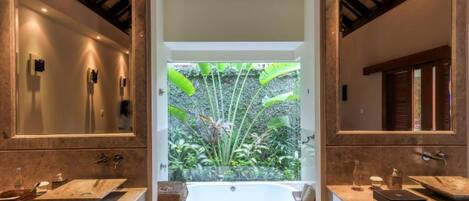 A bathroom with two sinks, a bathtub, and a large window with a view of greenery.