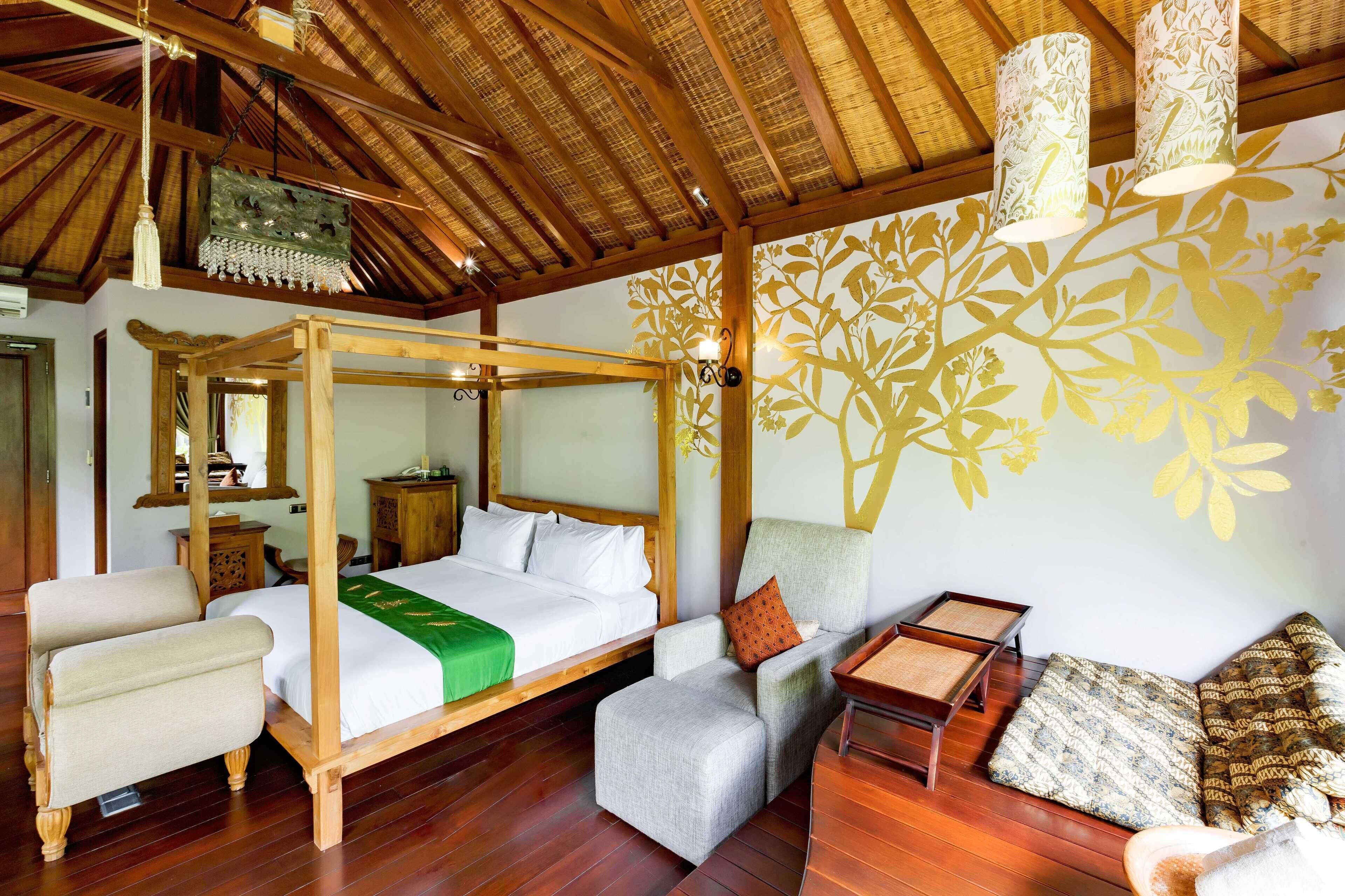 A room with a four-poster bed, a sitting area with a sofa and armchairs, and a decorative wall with a floral pattern.