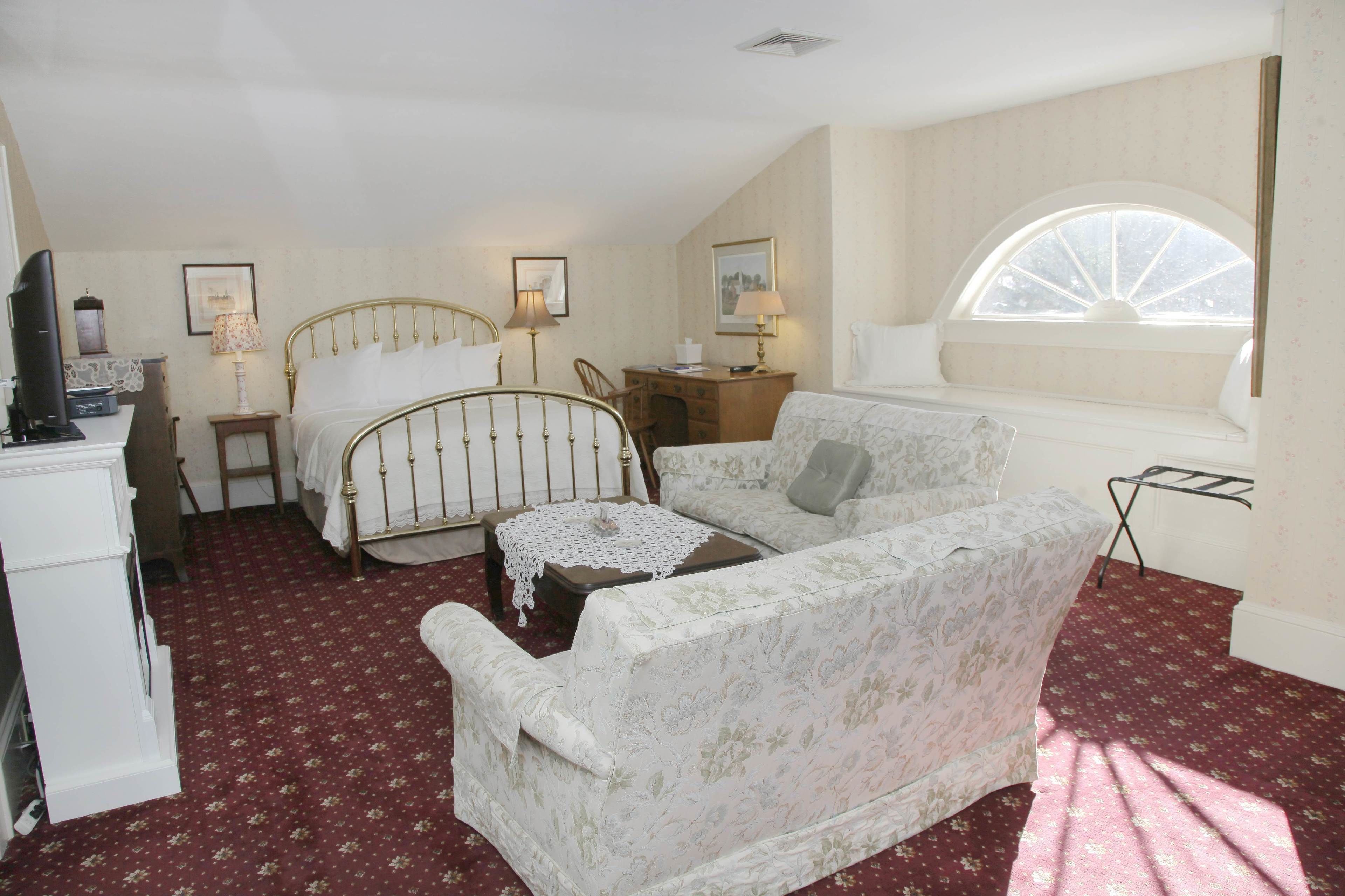 A bedroom with a bed, a sofa, a desk, and a window.
