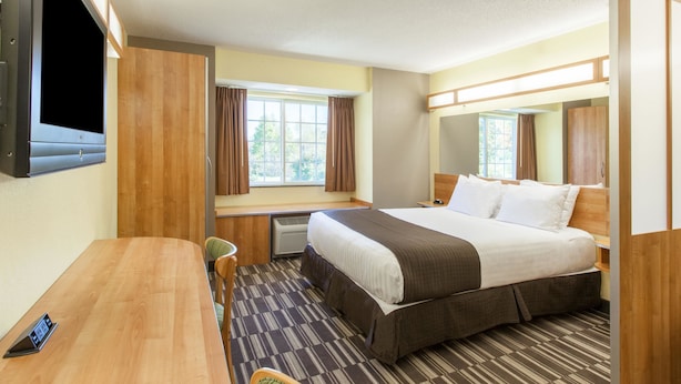 A hotel room with a bed, a desk, a chair, a TV, and a window with curtains. - Microtel Inn & Suites by Wyndham Johnstown (Johnstown)