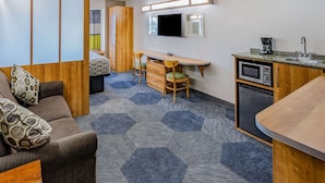 A compact hotel room with a kitchenette, a bed with a colorful curtain, a desk with two chairs, and a large mirror. - Microtel Inn & Suites by Wyndham Johnstown (Johnstown)