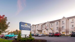 A Microtel Inn & Suites by Wyndham with a parking lot filled with cars, a building with multiple windows and a flag, and a clear sky. - Microtel Inn & Suites by Wyndham Johnstown (Johnstown)